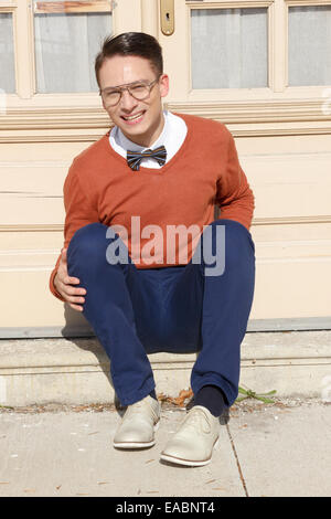 happy handsome man with glasses and sweater sitting on steps in front of house and posing , vintage retro photo Stock Photo