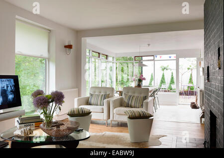 Pair of buttoned white armchairs in open plan living space with exposed brick wall and sun room Stock Photo