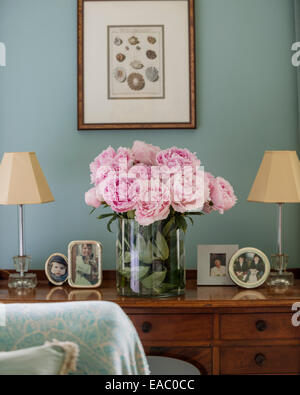 Pink peonies on antique dressing table with framed photos and small lamps Stock Photo