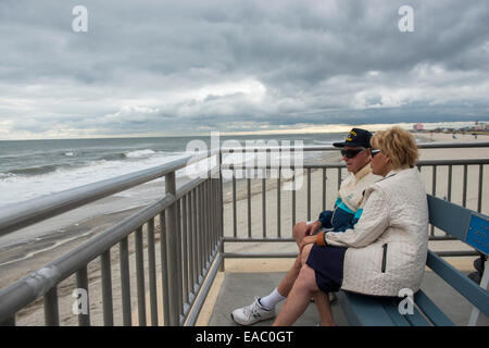 A retired couple sit on the boardwalk by the sea in Ocean City, New Jersey USA Stock Photo