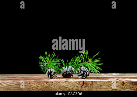 Three pine tree cones and twigs on an old wooden surface at black background Stock Photo