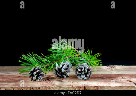 Three pine tree cones and a twig at an old weathered wooden table at black background Stock Photo