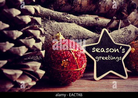 the text seasons greetings written in a star-shaped blackboard and some christmas balls, pinecones and a pile of logs in the bac Stock Photo