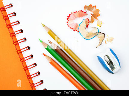 Four colorful pencils with sharpener and shavings on white notebook Stock Photo