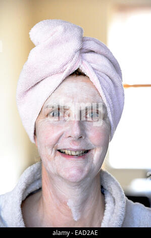 Middle aged woman female wearing a turban on wet hair and using a health and beauty face pack for the skin Stock Photo
