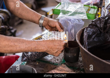 Market vendor sealing bag of freshly roasted black coffee beans for sell in indonesian market (Sulawesi). Unrecognizable person, Stock Photo
