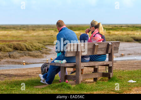 Family eating takeaway food on a bench at Moreston quay, Norfolk, UK Stock Photo