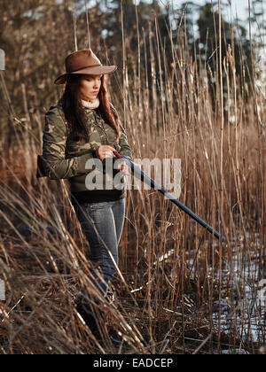 Waterfowl hunting, the female hunter loading the side by side shotgun, shore and reeds on background Stock Photo