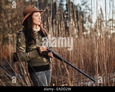 Waterfowl hunting, the female hunter loading the side by side shotgun, shore and reeds on background Stock Photo