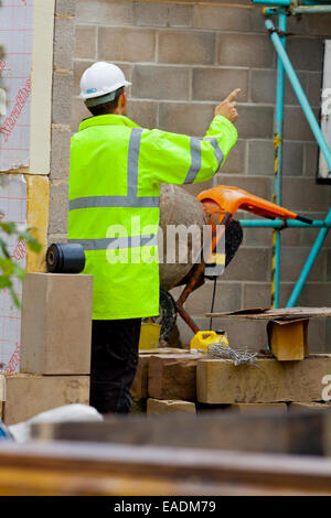 Builder working on a construction site wearing a high visibility jacket and white hard hat protective helmet Stock Photo