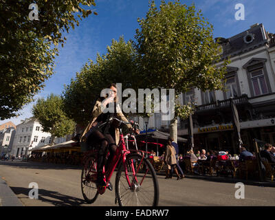 Young woman riding a bicycle in front of the cafes in Vrijthof square, Maastricht,The Netherlands, Europe Stock Photo