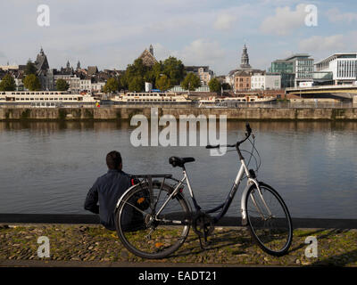 Person sitting next to a byclicle to the river Maas in Maastricht, The Netherlands, Europe Stock Photo