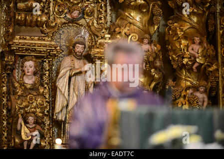 Statues of saints and angels on an ornate altar behind a catholic priest celebrating mass Stock Photo