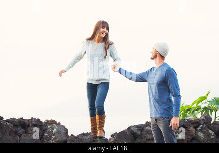 Happy Young Couple Having Fun Outdoors. Man helping attractive girlfriend over rock wall. Chivalry Concept, Romantic Date. Stock Photo