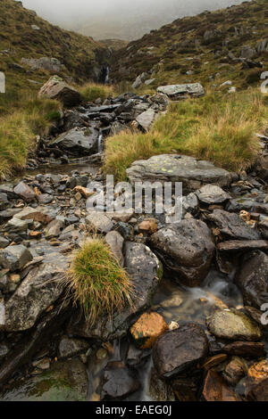 A stream creates a number of mini waterfalls as it flows into Llyn Idwal on a misty morning in Snowdonia, Gwynedd, North Wales Stock Photo