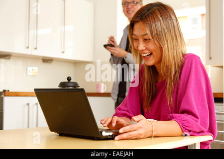 Mixed race couple using wireless devices - a laptop and a smart phone with stylus - communicating over the internet. Stock Photo