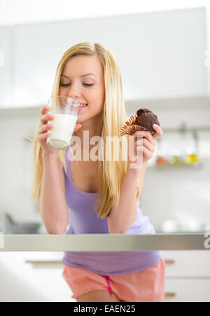 Young woman having muffin with milk in kitchen Stock Photo
