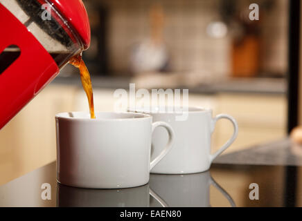 Ground coffee being poured from a red cafetiere into two white cups Stock Photo