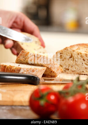 Loaf of seeded rye bread in a domestic kitchen - man spreading slice, focus on remaining slices Stock Photo