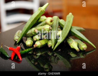 a stack of okra, or lady's fingers, reflected in a black granite worktop or chopping board with some chillies Stock Photo
