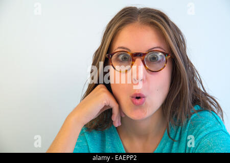 Young long-sighted woman wearing eyeglasses, looking at the camera astonished. Close view. Stock Photo