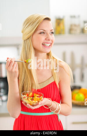 Happy young woman eating fruits salad in kitchen Stock Photo