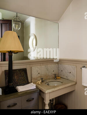 Old basin and taps set into a marble top with marble panels in guest cloakroom with large mirror Stock Photo