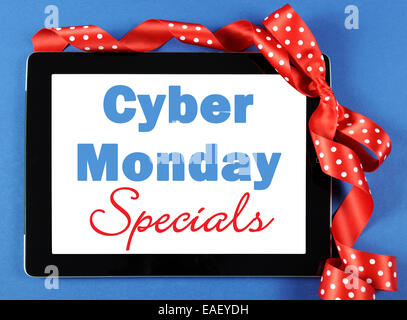 Cyber Monday Specials sale shopping sign on black computer tablet device on blue background with red polka dot ribbon. Stock Photo