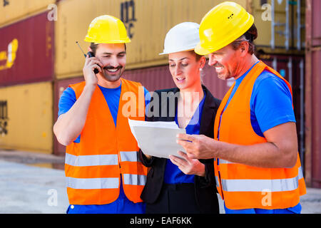 Worker and manager of shipment company discussing freight or shipment documents, one man is using phone or walkie-talkie Stock Photo