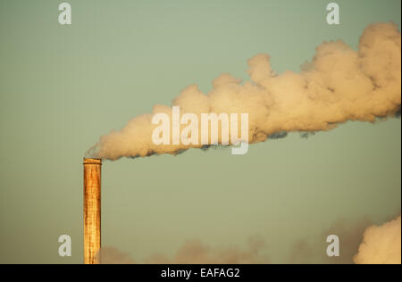 old rusty smokestack with plume of smoke lit by early morning light Stock Photo
