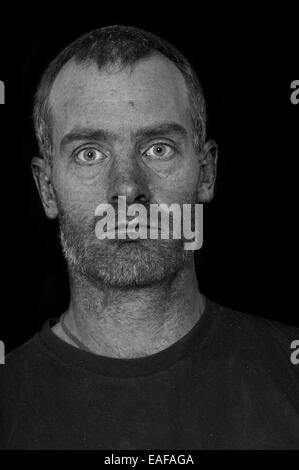 portrait of a rugged grizzled middle aged man with black t-shirt on black background processed to show skin texture and flaws Stock Photo