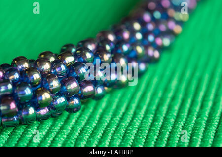 Knitted necklace from blue-green beads on green fabric Stock Photo
