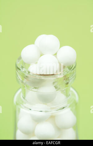 Macro closeup image of homeopathic medicinal pills in a bottle on a green background. Stock Photo