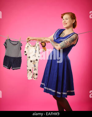 The expectant woman hang up baby clothes to clothesline Stock Photo