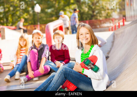 Girl sits in front with skateboard and other kids Stock Photo