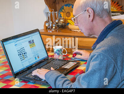 Retired man solving a crossword puzzle using a laptop computer. Stock Photo
