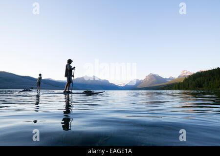 A man and woman stand up paddle boards (SUP) on Lake McDonald in Glacier National Park. Stock Photo