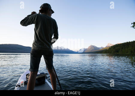 A woman stand up paddle boards (SUP) on Lake McDonald in Glacier National Park. Stock Photo