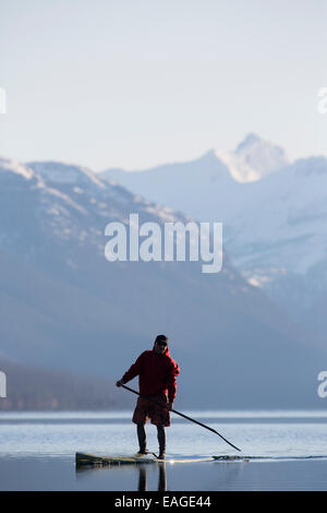 A man stand up paddle boards (SUP) on a calm Lake McDonald in Glacier National Park. Stock Photo