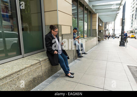 Woman and a man leaning against window / wall and looking at their smartphones Stock Photo