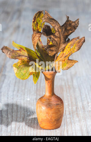 Small wooden vase with autumn leaf. White wooden background Stock Photo