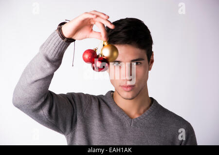 Handsome young man holding Christmas tree balls in front of his face, looking at camera on white background Stock Photo