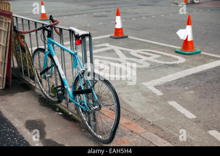 Bicycle secured to railings next to cycle lane with damaged rear wheel Stock Photo