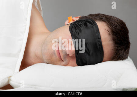 Man with Sleeping mask and earplugs lying in bed Stock Photo