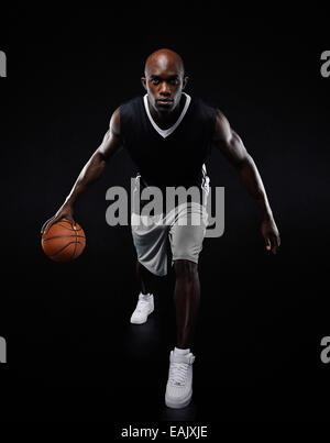 Full length portrait of young basketball player playing on black background. Fit African male athlete playing basketball. Stock Photo