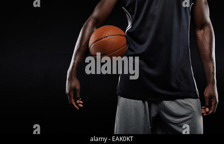 Cropped image of Afro-American basketball player holding a ball against dark background Stock Photo