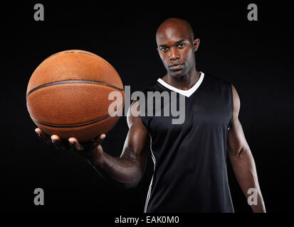 Portrait of confident young basketball player with a ball looking at camera against black background Stock Photo