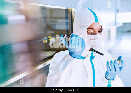 Scientist in clean suit pipetting sample into Petri dish in laboratory Stock Photo