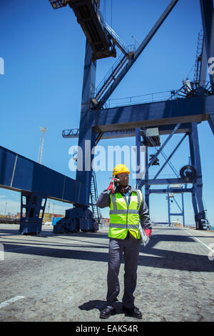 Worker talking on cell phone near cargo crane Stock Photo