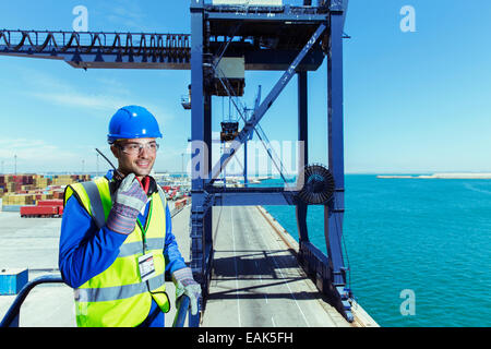 Worker using walkie-talkie on cargo crane at waterfront Stock Photo